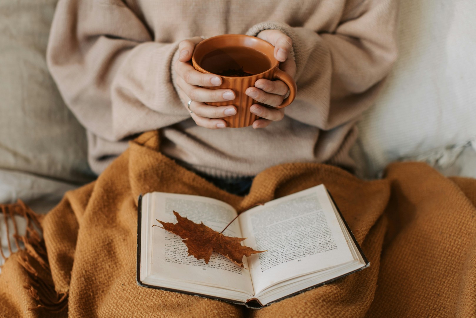 A person in bed holding a cup of tea and reading a book with a leaf in it